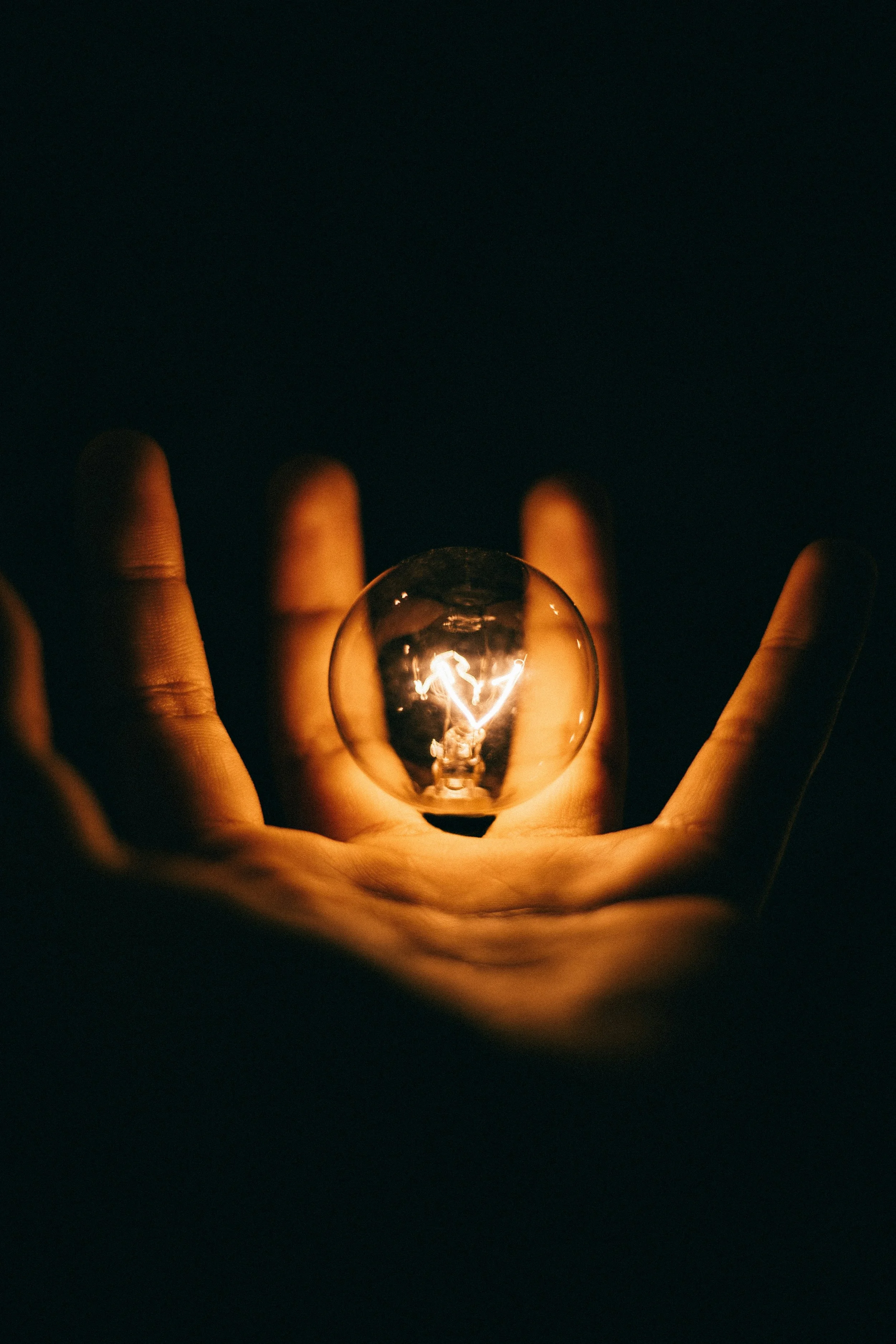 Hand holding a glowing light bulb in the dark, with a heart shape inside the bulb.
