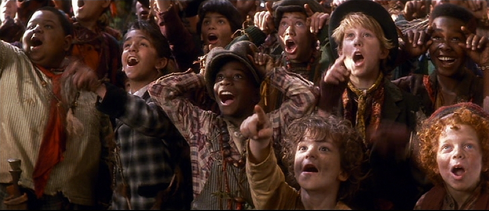 A group of children, with various ethnicities and hair types, excitedly watching something. They have open mouths, wide eyes, and are pointing or raising their hands, showing surprise or awe.