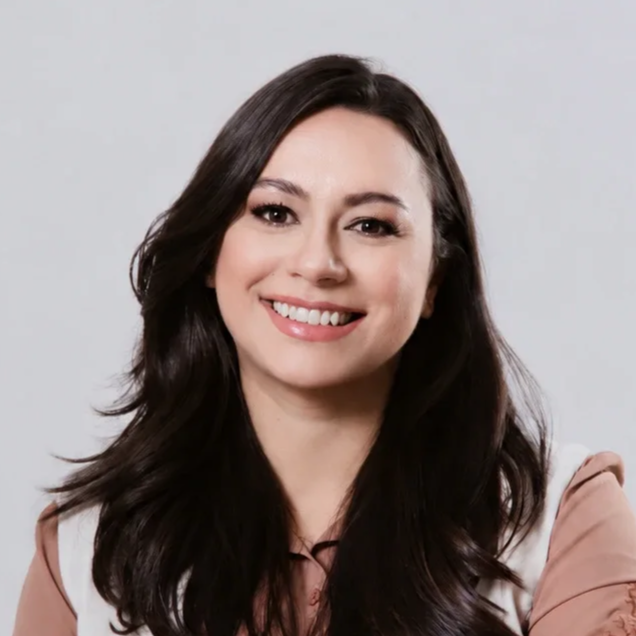 Mulher com cabelo castanho escuro, sorrindo, em fundo neutro.