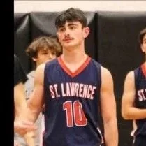 Teen basketball player in St. Lawrence jersey numbered 10, standing on a court with other players in the background.