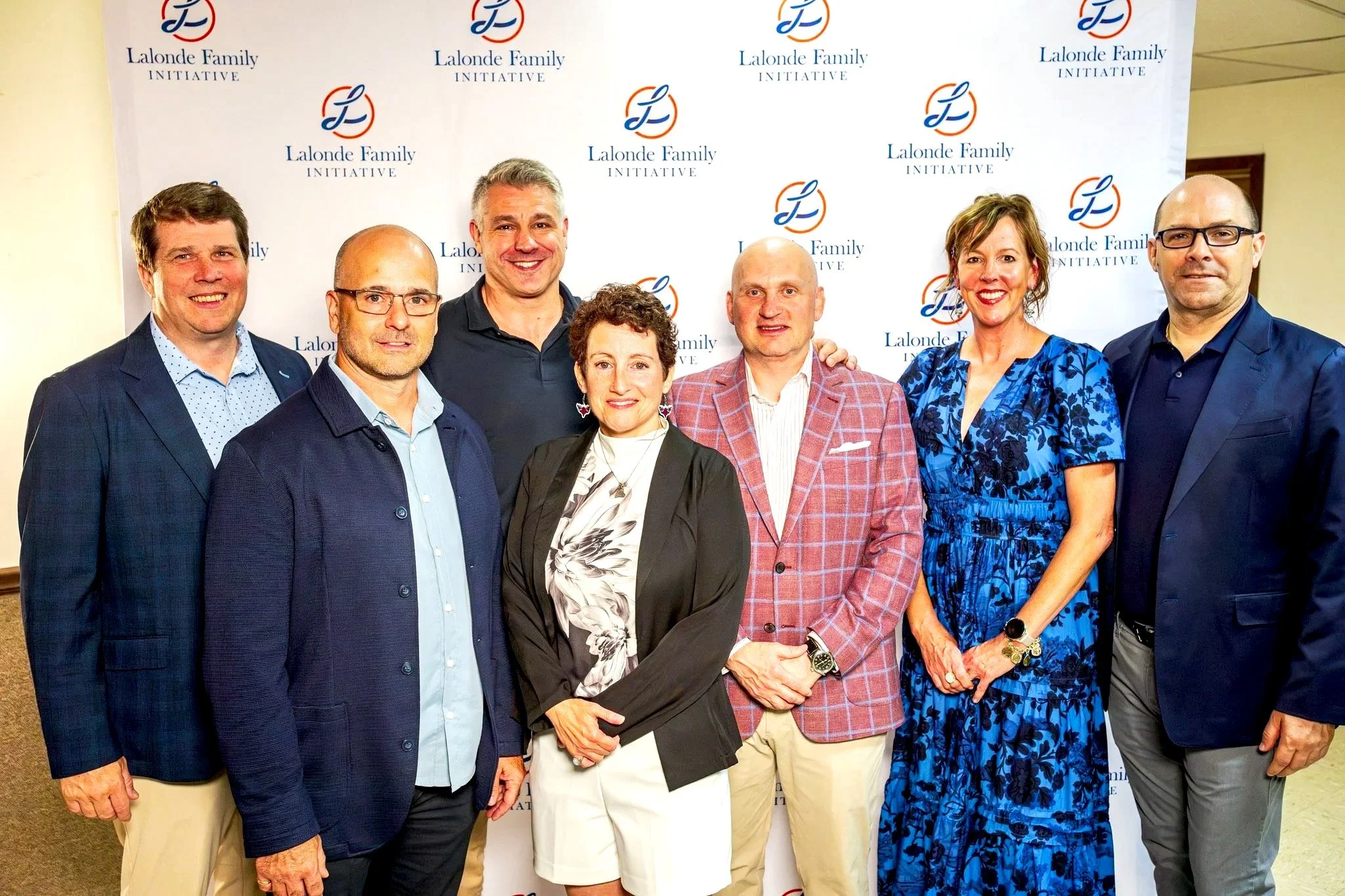 Group photo of nine people standing in front of a background with the logo and text "Lalonde Family Initiative." They are dressed in business casual attire, smiling for the camera.