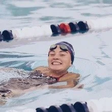 Young woman swimming in a pool, smiling, wearing goggles.