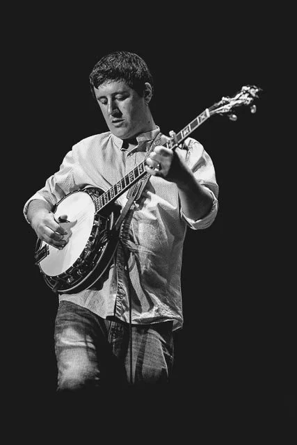 A young man playing an acoustic guitar on stage, black and white photo.