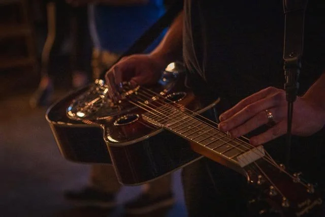 A person playing an acoustic guitar in a dimly lit setting.
