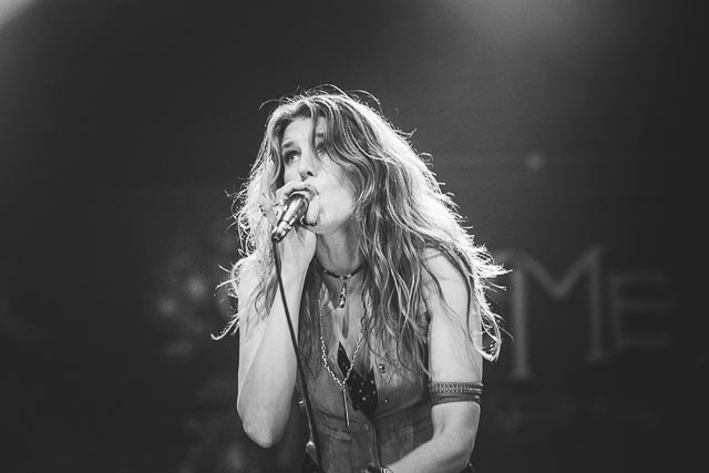 A woman with long, wavy hair singing into a microphone on stage.