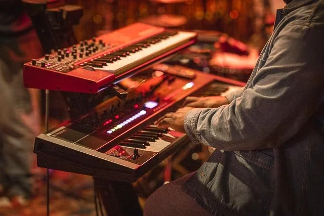 Close-up of a person playing a keyboard at a live music event, with another keyboard above it.