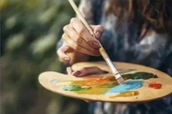 Person painting on a wooden palette outdoors with a brush.
