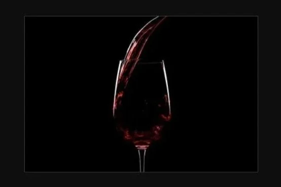 A glass of red wine being poured with streaks of red liquid in a dark background