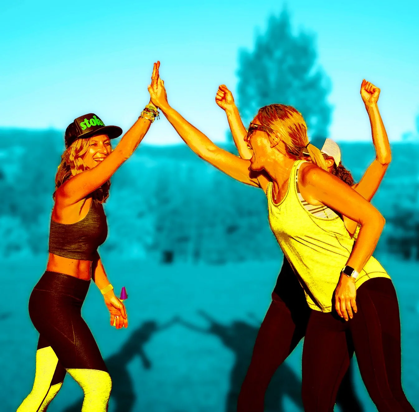 Two women high-fiving outdoors on a sunny day with a blurred tree in the background.
