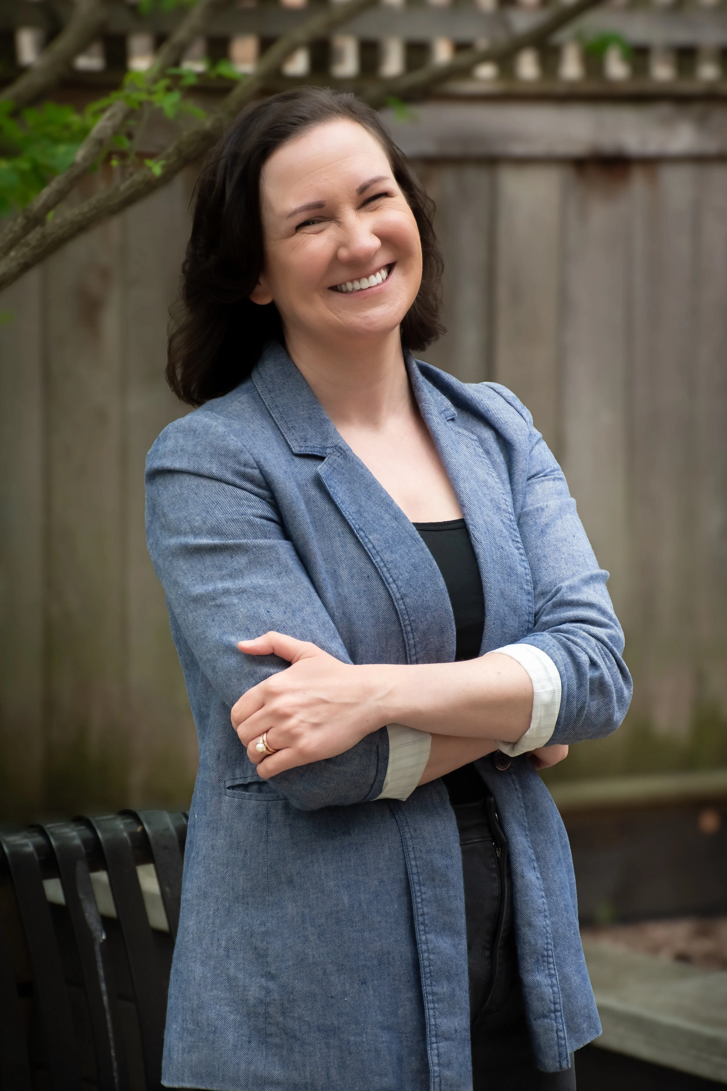 A fractional Chief Operating Officer in a blue blazer stands smiling in front of a green tree in a Chicago park. Promotional image for Make a Plan and Execute fractional Chief Operating Officer offerings