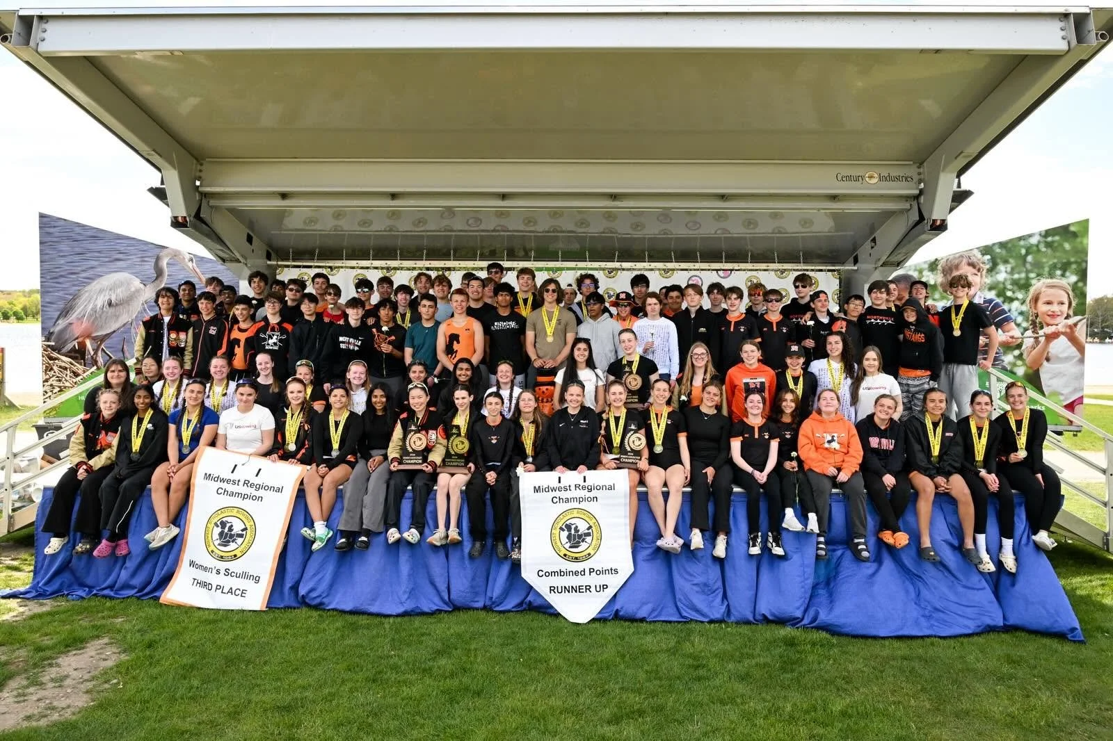 A group of rowers pose with their championship trophy and banners.