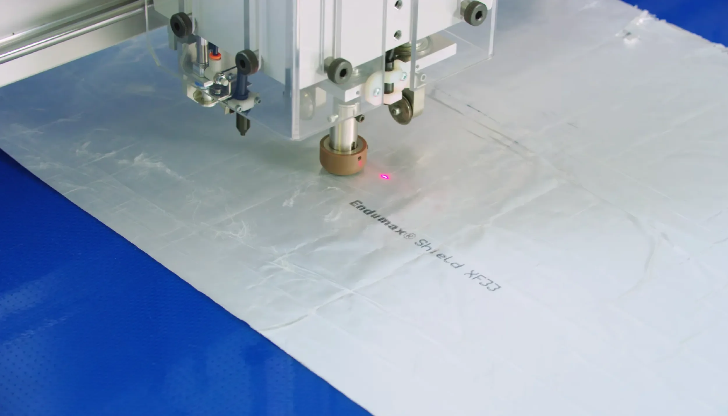 Close-up of a manufacturing machine placing an endface on a fiber optic connector, with a pink laser beam aiming at the connector on a clear plastic surface, with text partially visible.