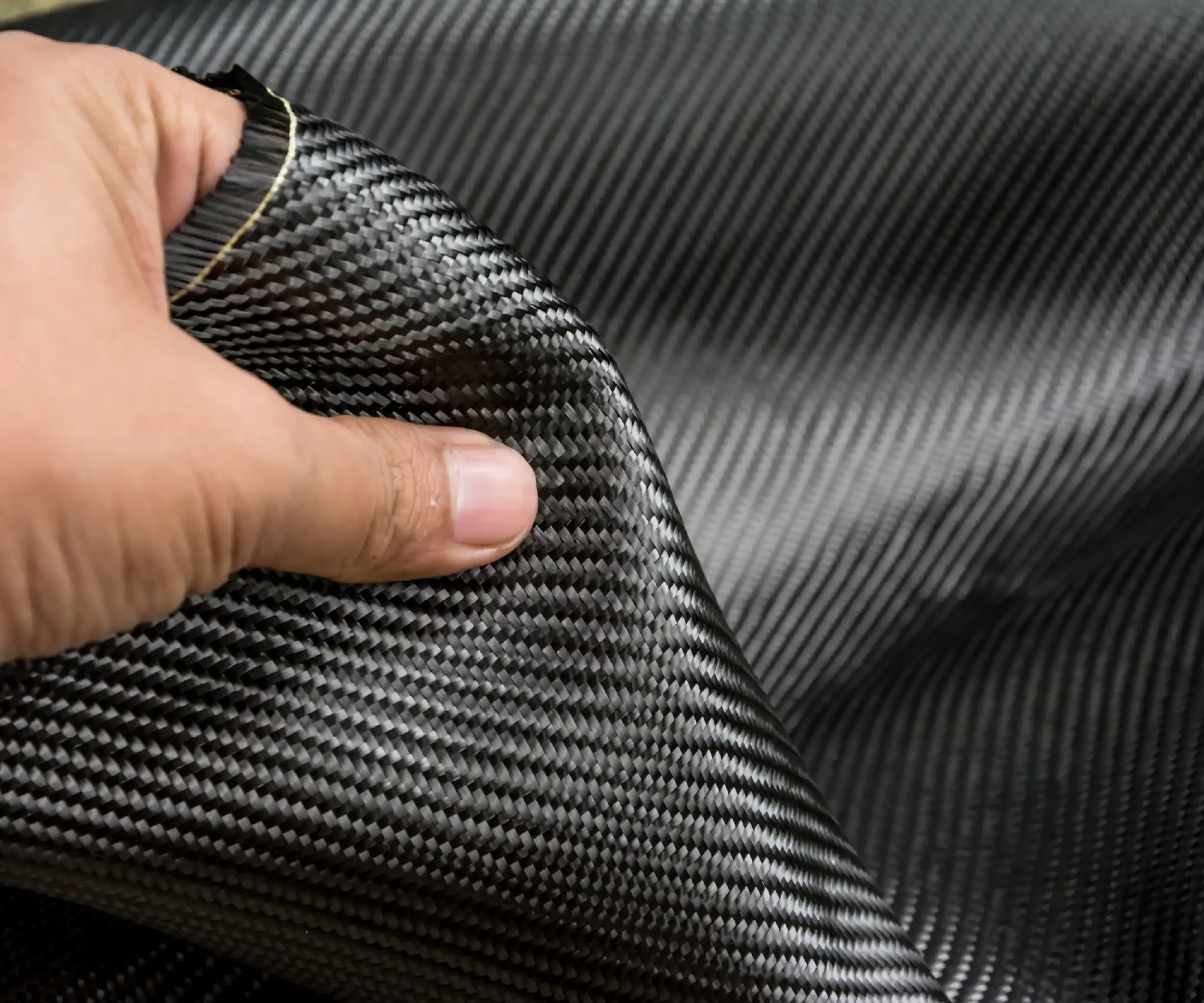 Close-up of a person's hand holding a piece of black and gray carbon fiber fabric.