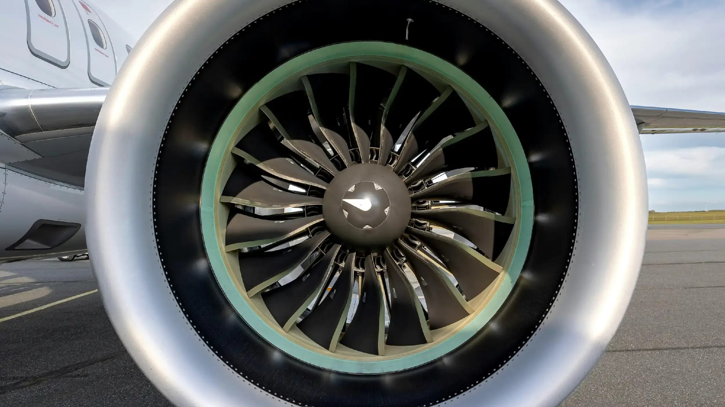 Close-up of a jet engine's intake with visible fan blades and aircraft wing in background.