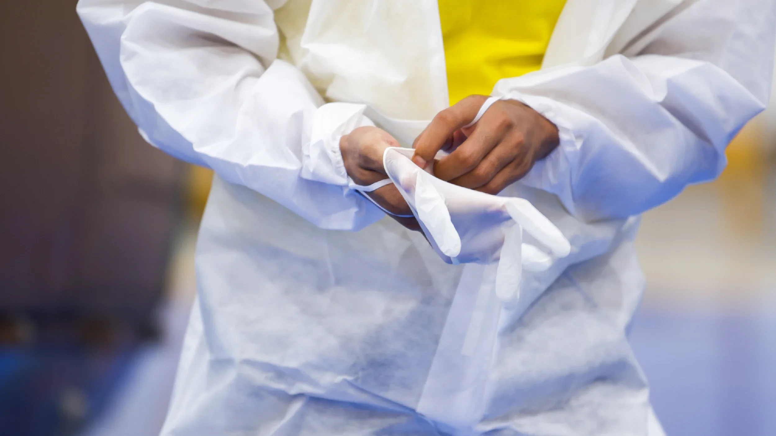Person wearing white protective suit putting on gloves.