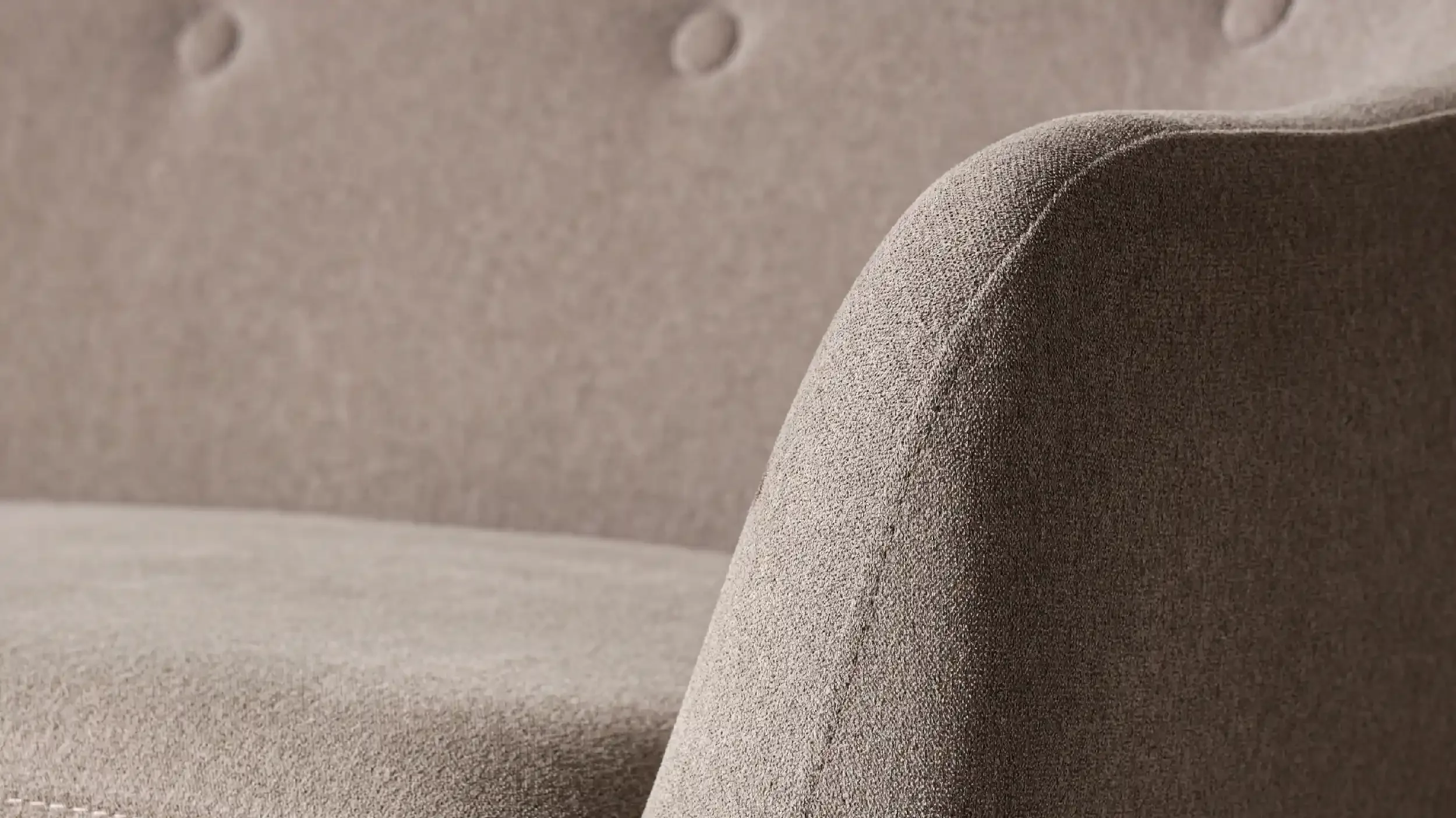 Close-up of a textured, taupe-colored upholstered armrest on a piece of furniture, with a soft fabric surface.