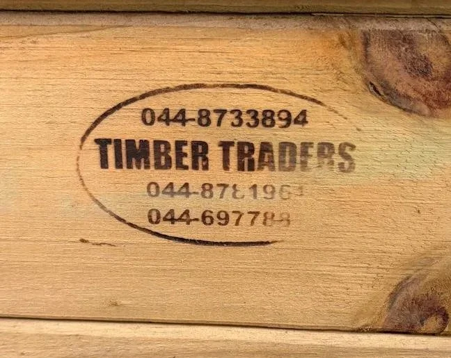 Close-up of a stamped logo on a wooden surface for Timber Traders, including phone numbers.