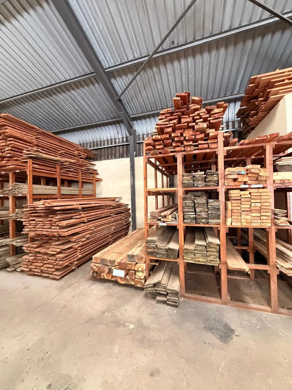 Stacks of wooden planks and lumber stored on metal shelves inside a warehouse.