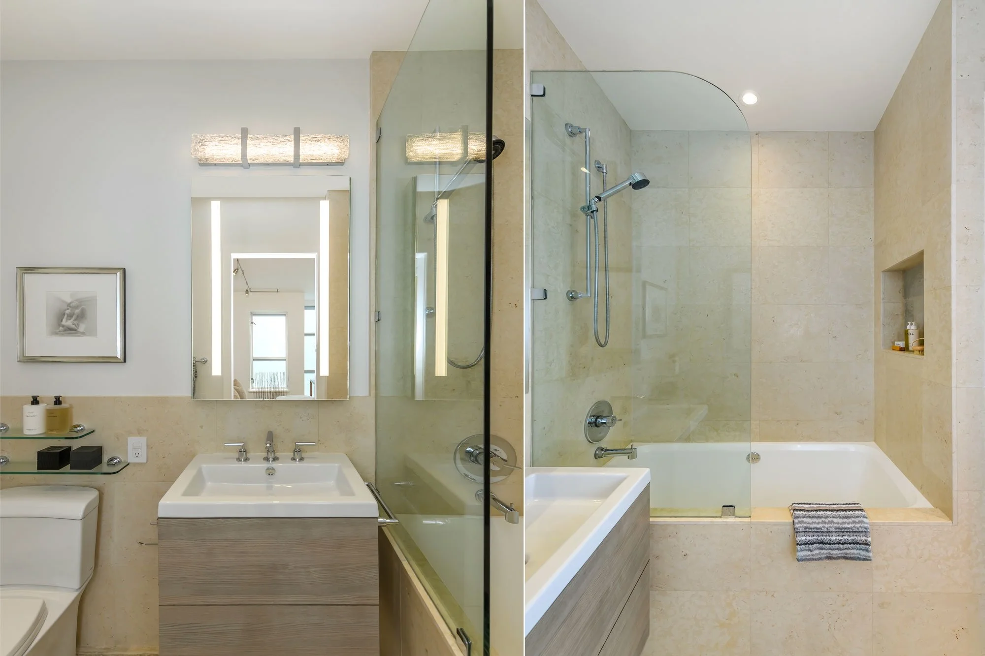 The image shows a modern bathroom with a large mirror above a white sink, beige tiled walls, and a glass-enclosed shower with a showerhead and fixtures. There is a small built-in shelf in the shower holding toiletries and a striped towel on the floor