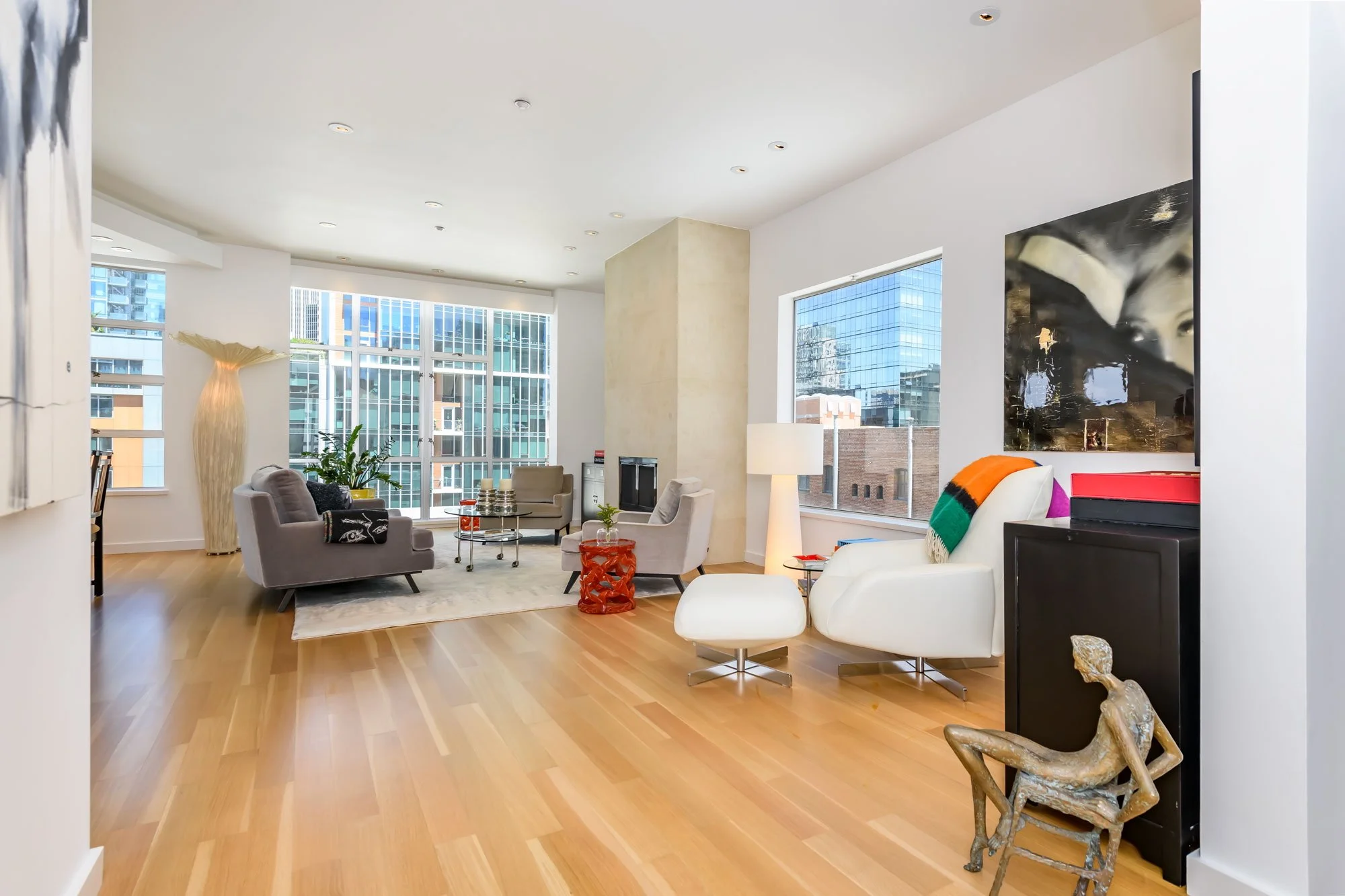 Modern living room with large windows, white walls, and hardwood floors, furnished with multiple chairs, a sofa, and decorative items.
