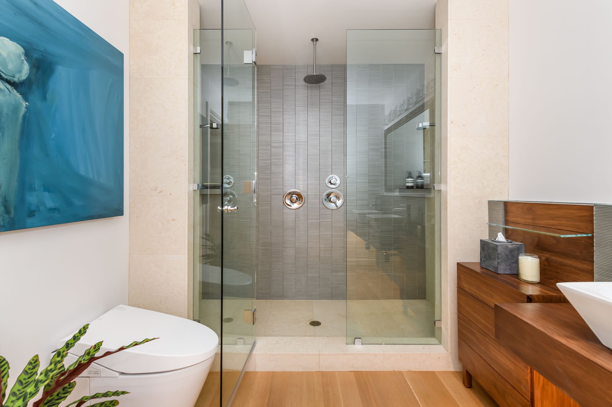 Modern bathroom with a glass-enclosed shower, wall-mounted showerhead, and wooden vanity with decorative items.