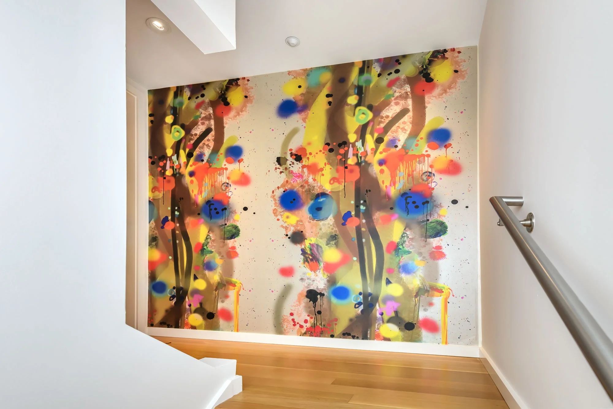 A colorful abstract mural painted on a wall, seen from the top of a staircase with a wooden floor and a metal handrail.