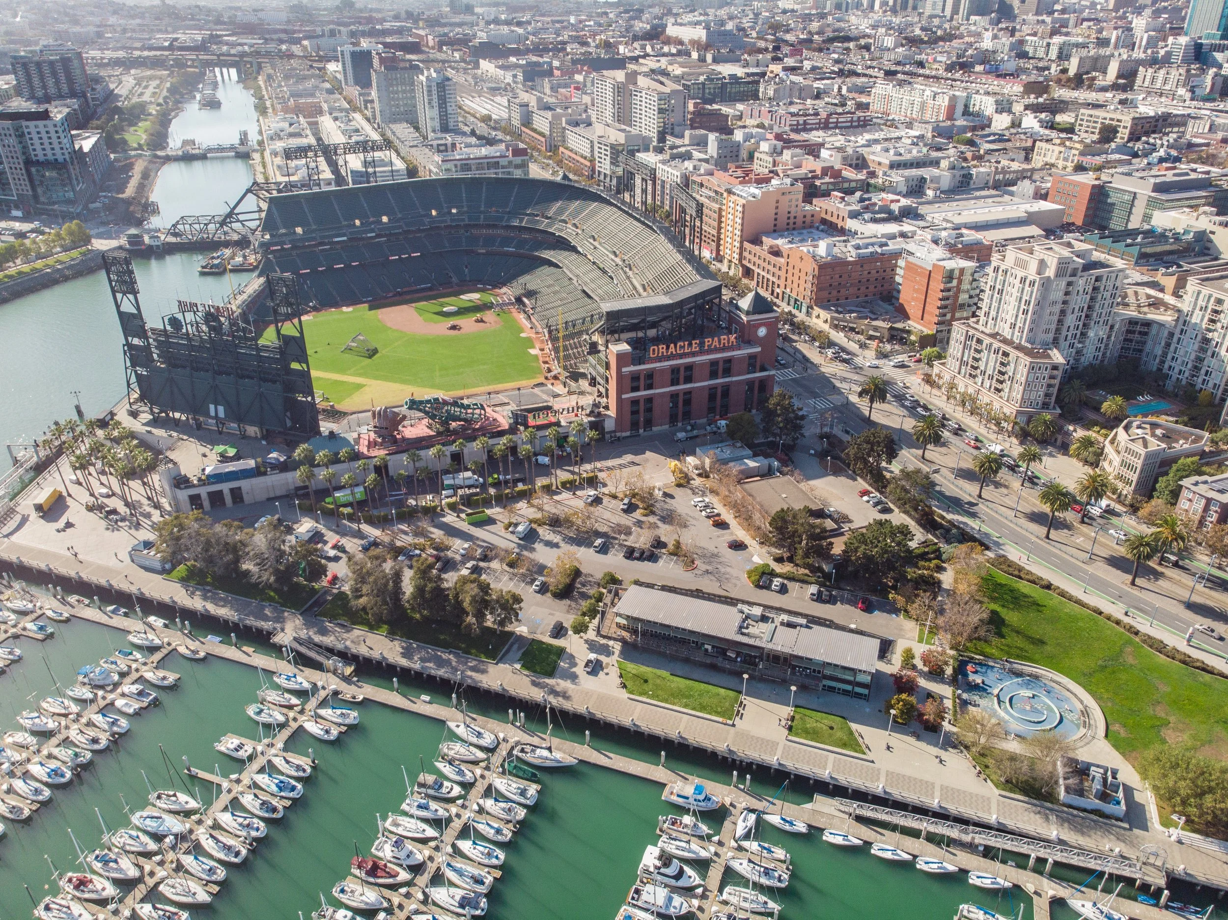 An aerial view of Oracle Park baseball stadium with surrounding cityscape and marina filled with boats.