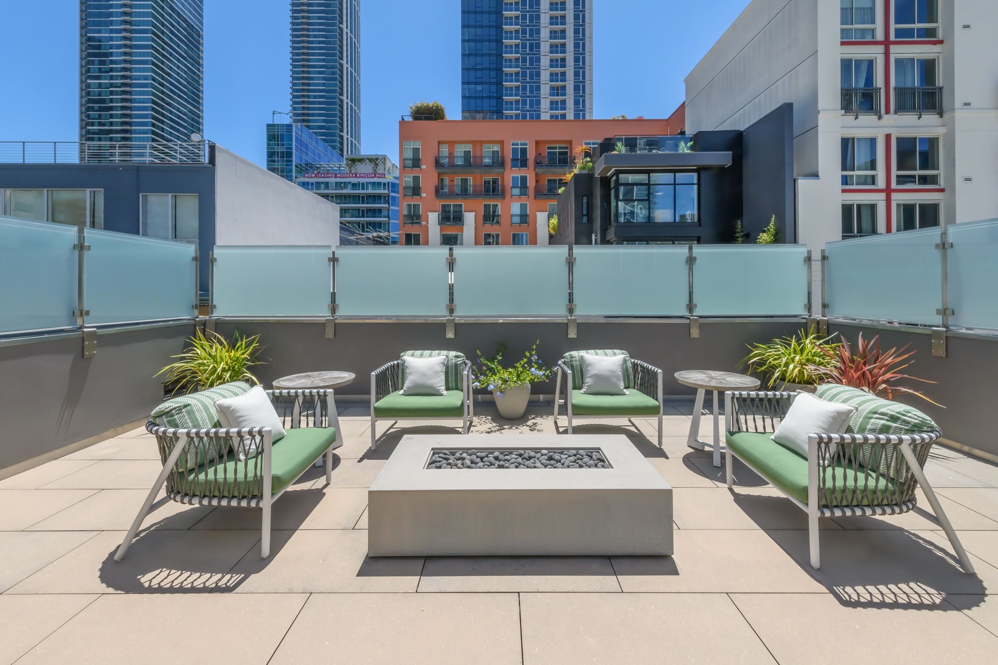 Balcony with modern outdoor furniture, plants, and cityscape view with high-rise buildings in the background.