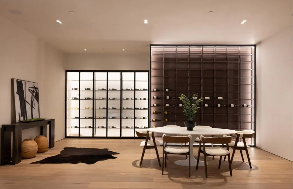 Minimalist dining room with a round table, six chairs, a potted plant centerpiece, and a wine display wall with backlit shelves.