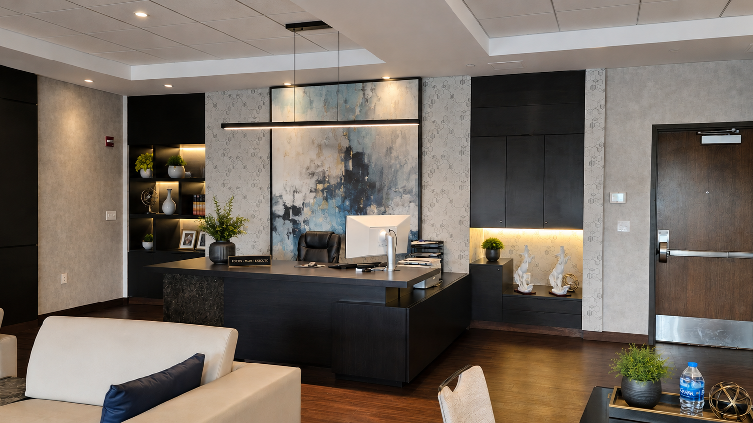 Modern office reception area with a black desk, computer, decorative items, and a beige sofa with a navy pillow.