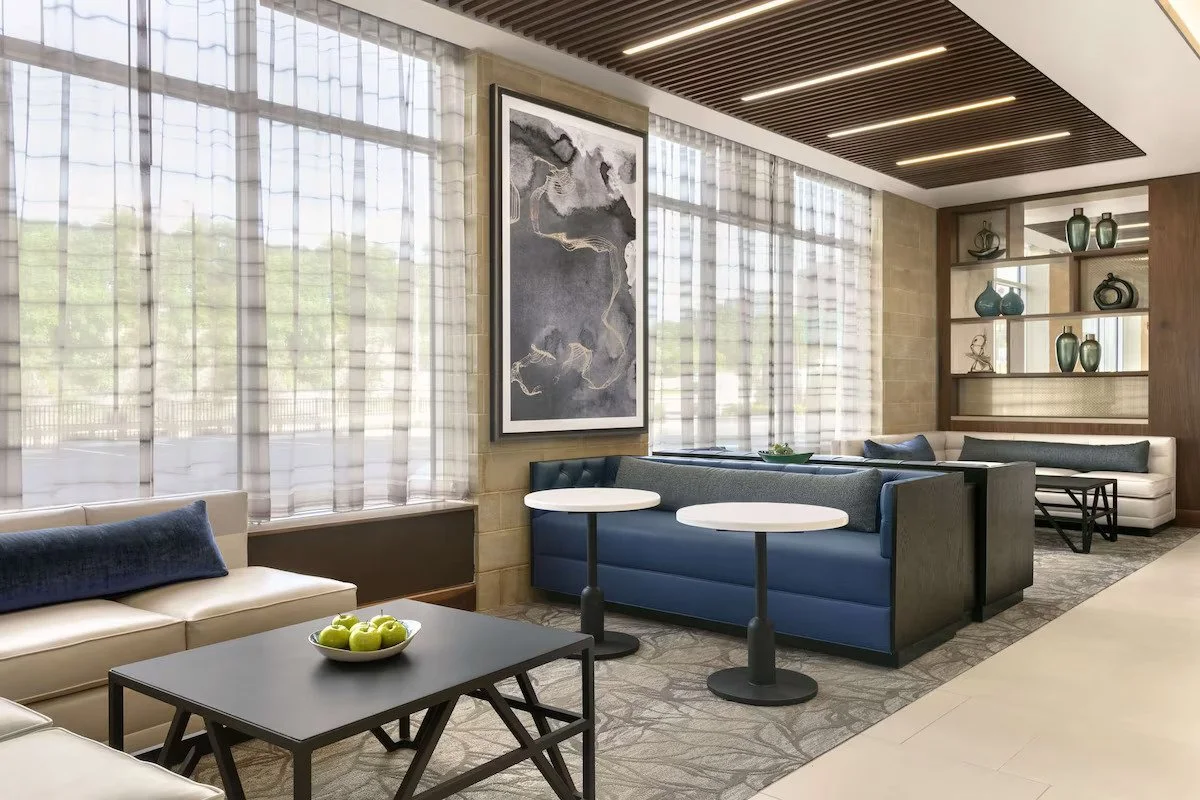 Modern hotel lobby with large windows, abstract wall art, blue and white couches, and decorative vases on open shelves