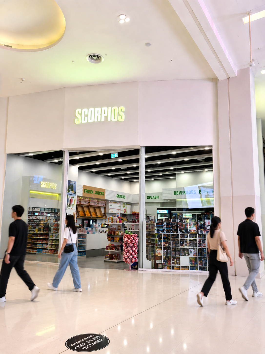 People walking past a store named 'Scorpios' in a mall, with shelves of snacks, frozen juices, and drink items visible inside.