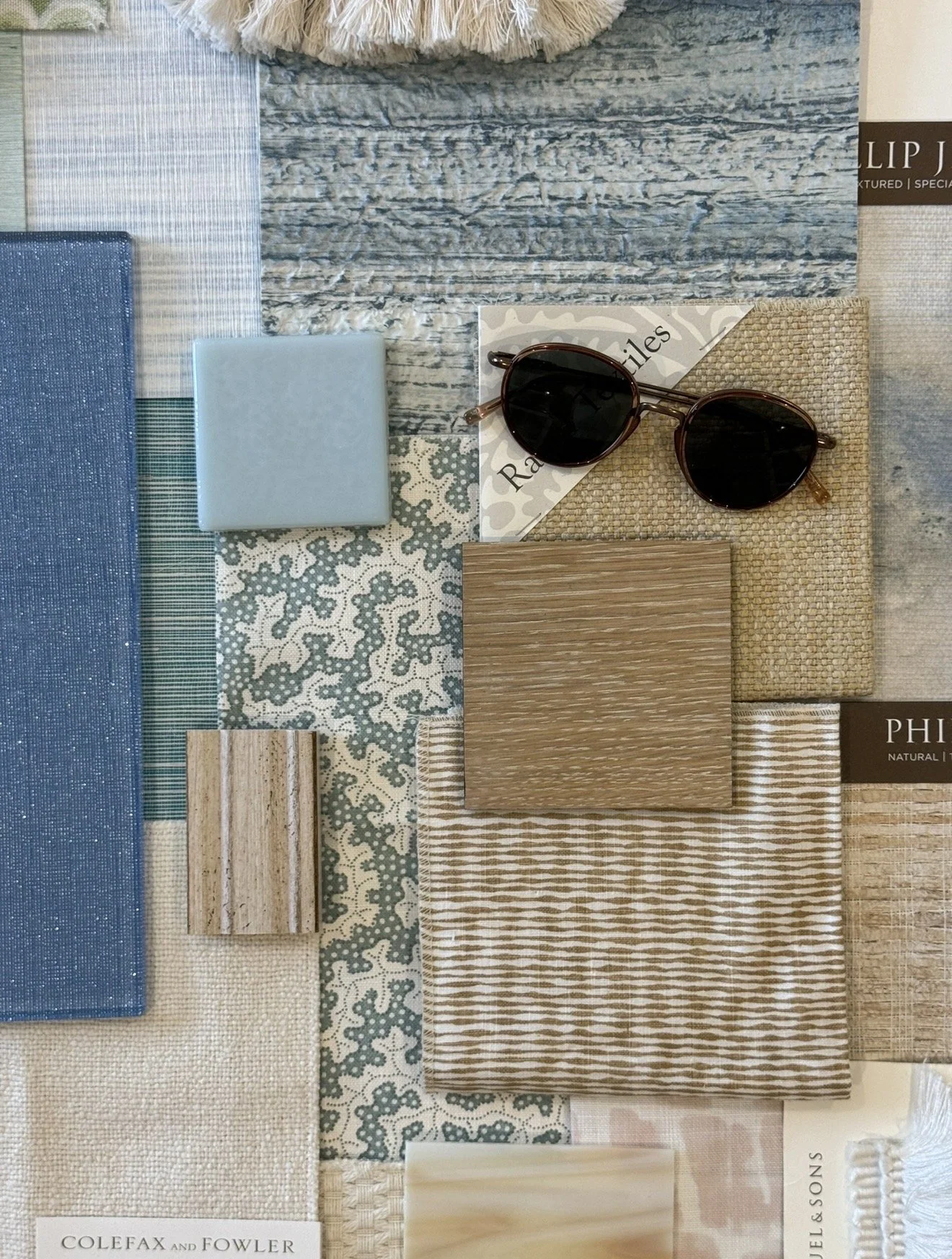 Palm Beach. A collection of fabric and material samples in various colors, textures, and patterns, with a pair of dark sunglasses placed on top of a sample.