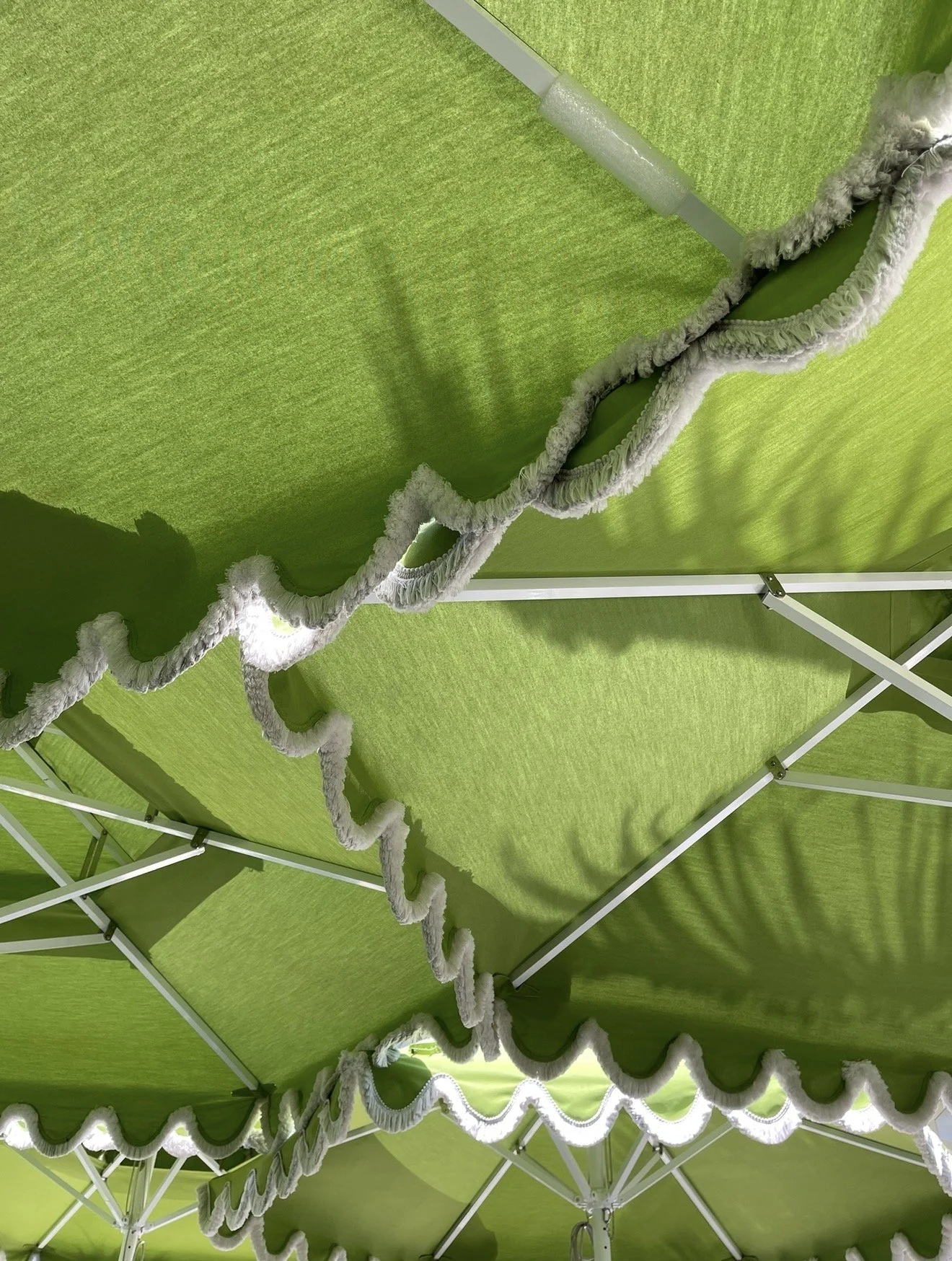 Palm Beach. Close-up view of a green canopy or tent roof with scalloped edges and white trim, supported by metal frame structures.