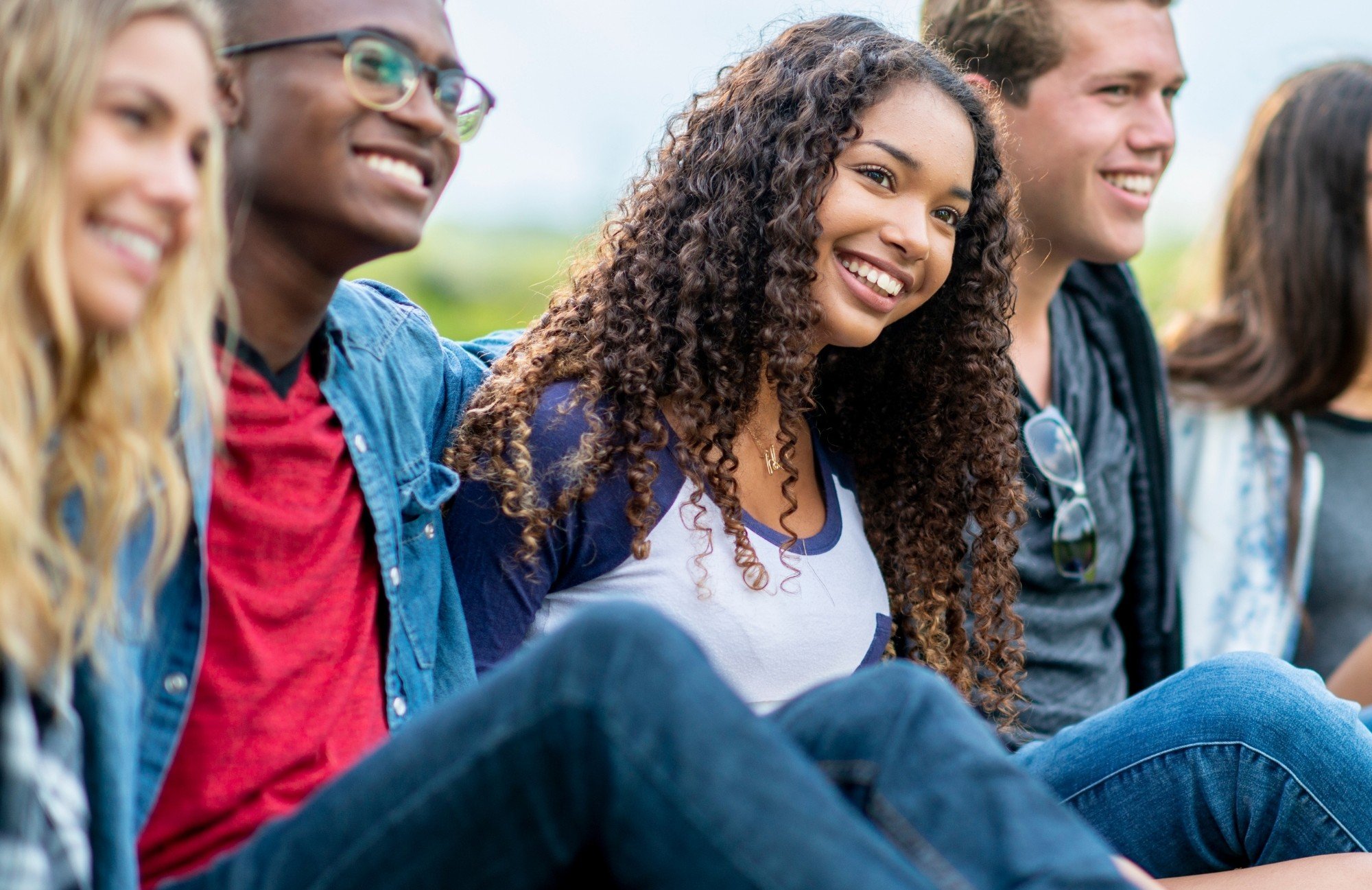 A group of smiling teenagers and young adults sitting outdoors together, representing autism services across every stage of life in Thomasville, Forsyth County, and Davidson County, NC.