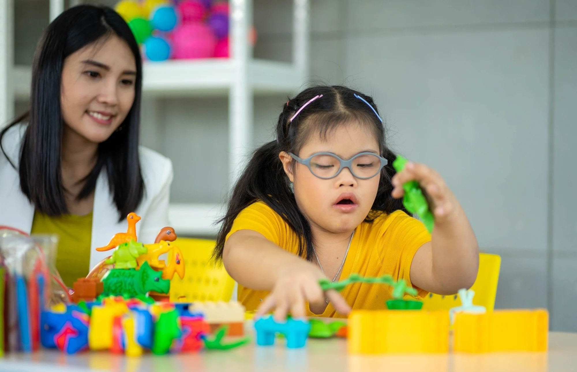 A young girl working on developmental skills with colorful building blocks next to an autism services team member in Davidson County, North Carolina.