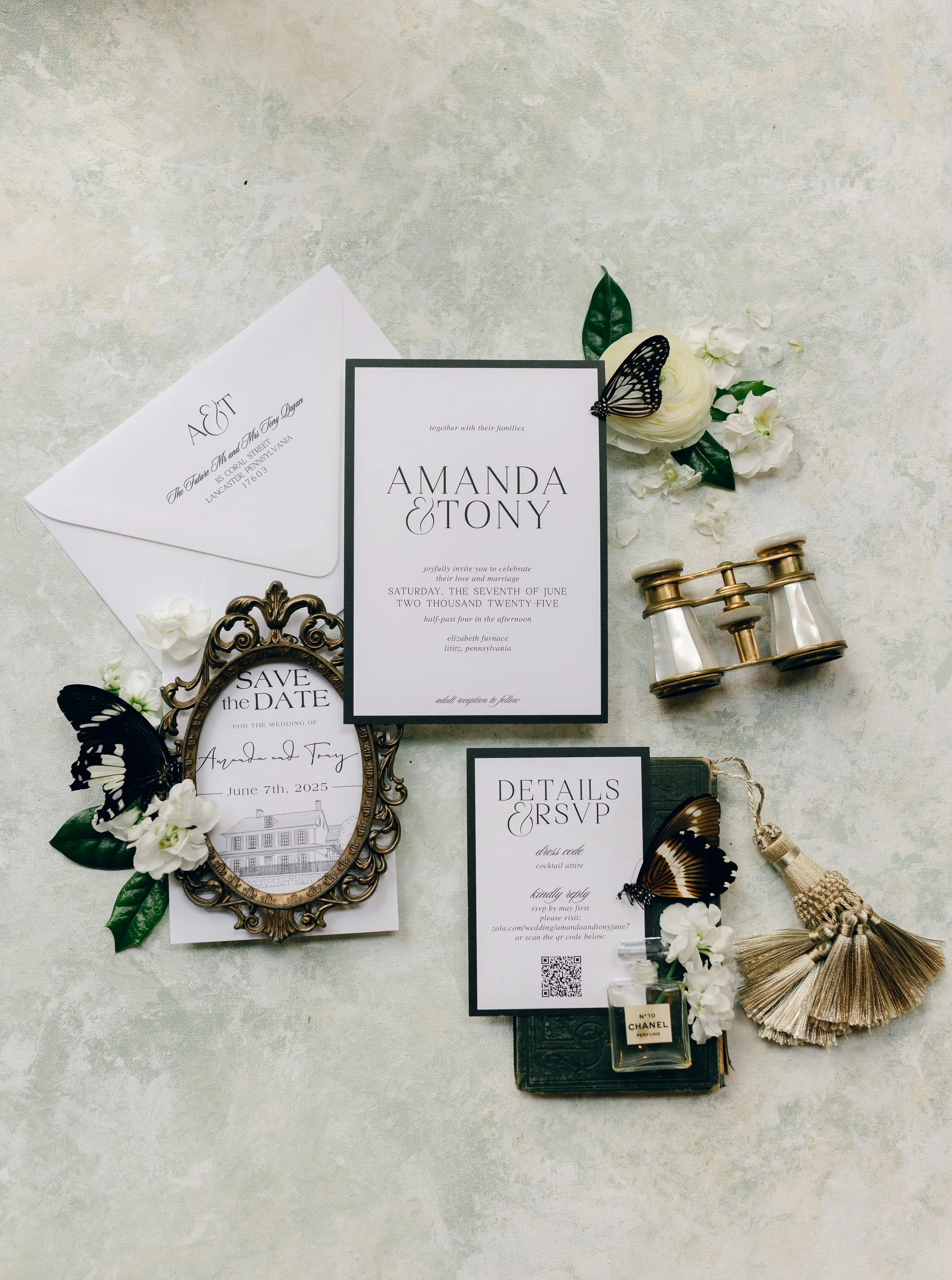 Wedding invitation suite with floral accents, butterflies, vintage hand mirror, and perfume bottles on a light textured surface.