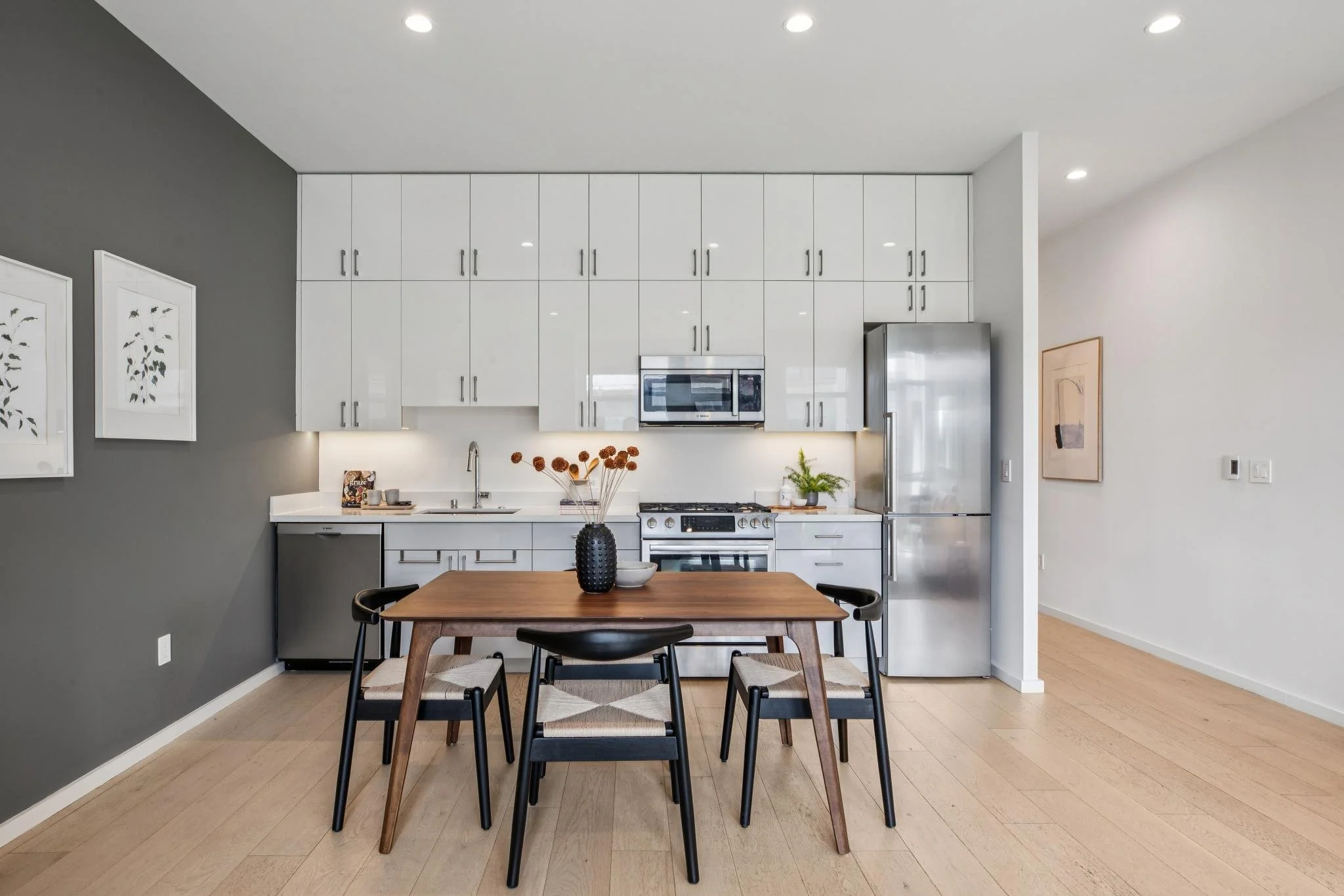 Modern kitchen with white cabinets, stainless steel appliances, and a wooden dining table with black chairs.