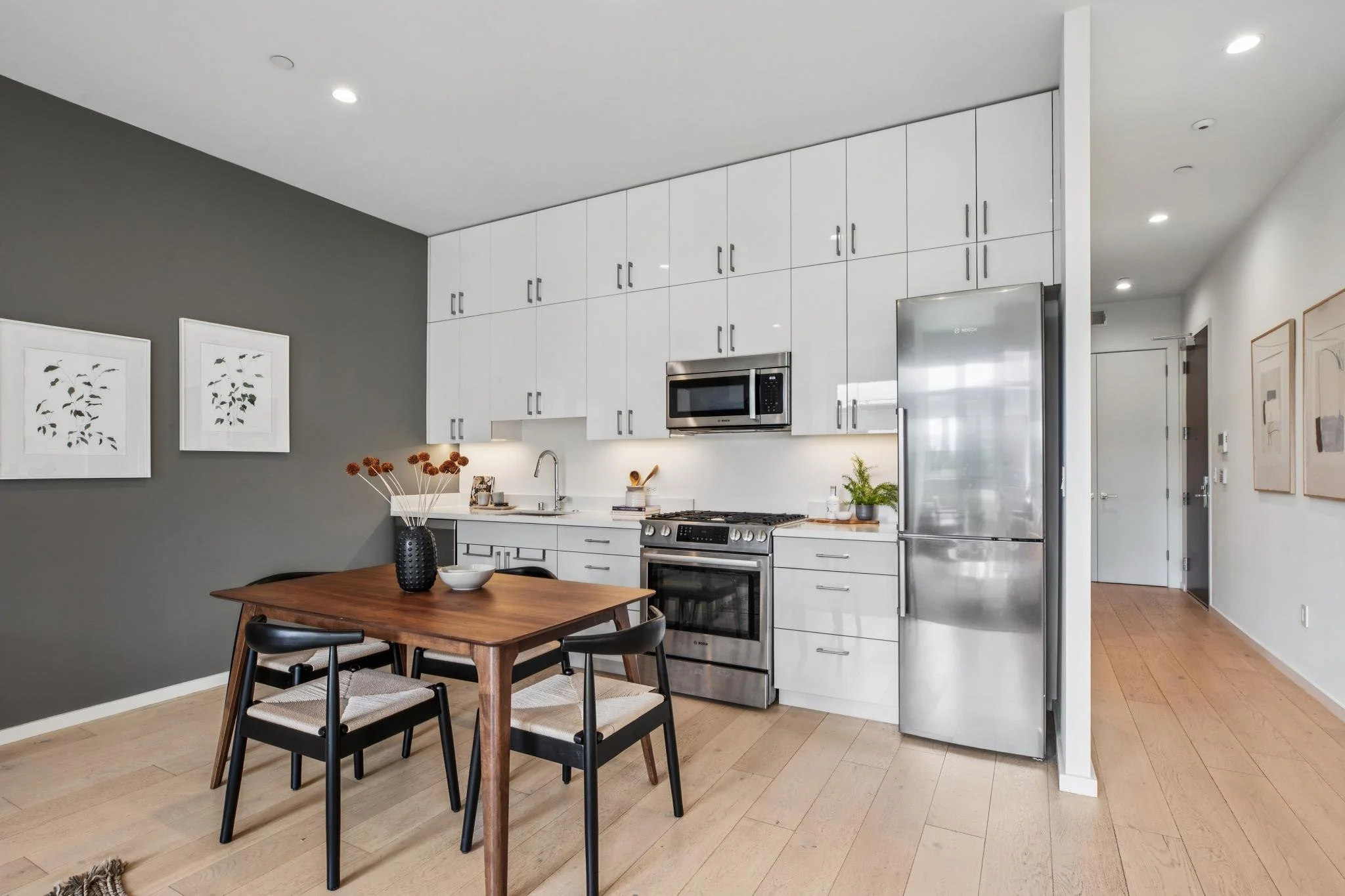 Modern kitchen with white cabinets, stainless steel appliances, and a wooden dining table with black chairs.