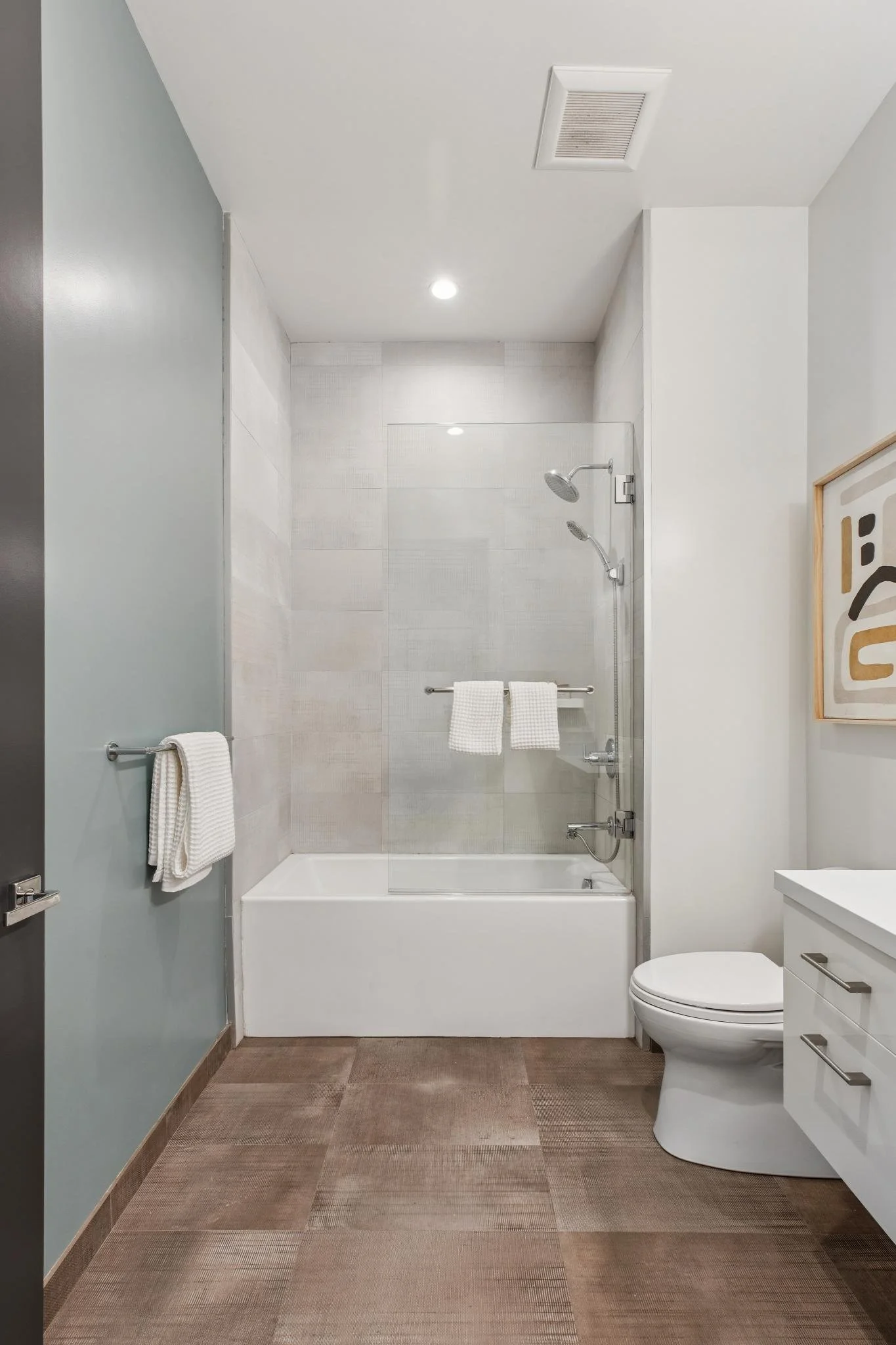 Modern bathroom with a bathtub and shower, white walls, wooden flooring, and a white vanity
