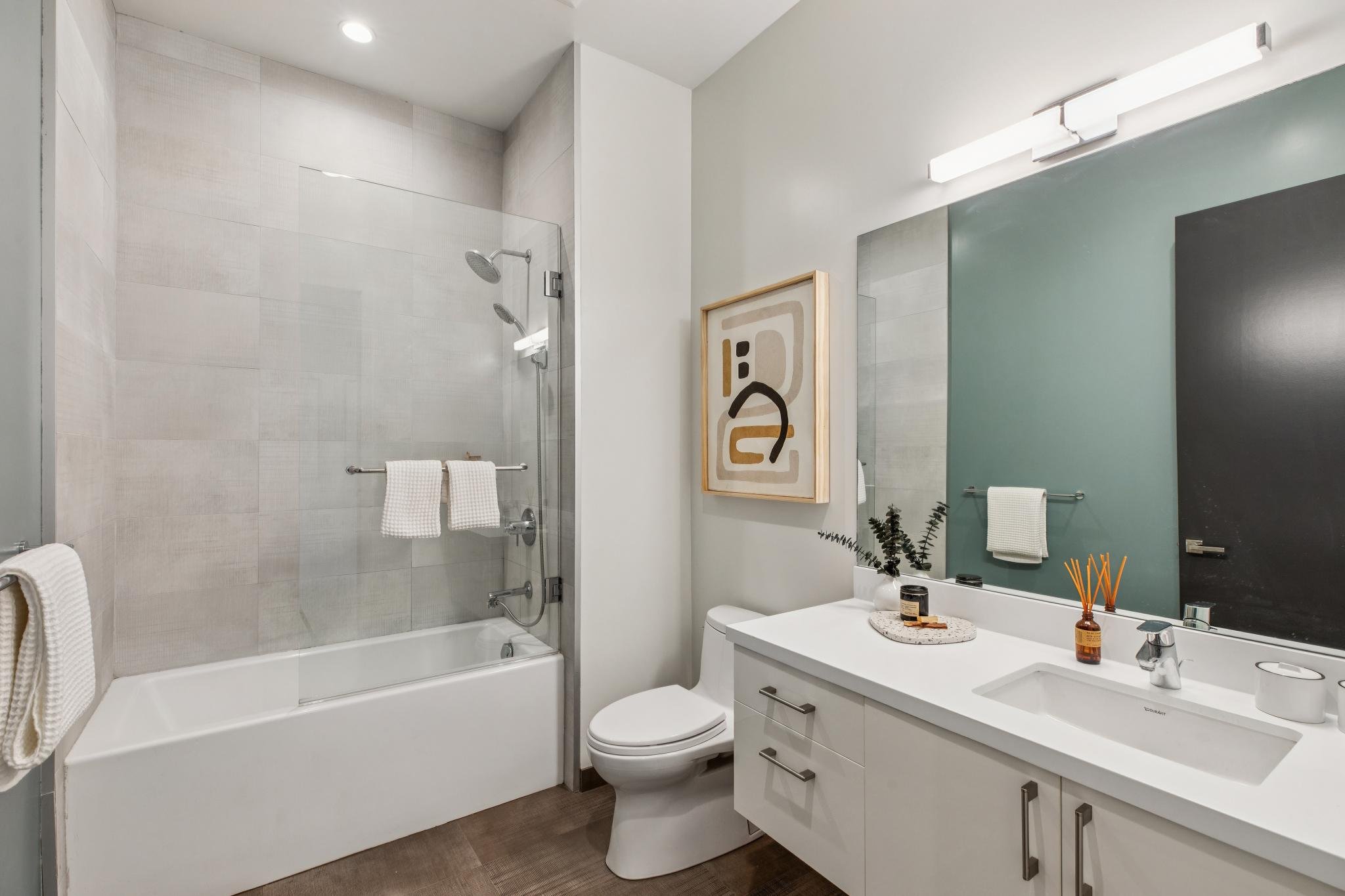 Modern bathroom with a glass-enclosed shower, white vanity with mirror, decorative artwork, and potted plant.