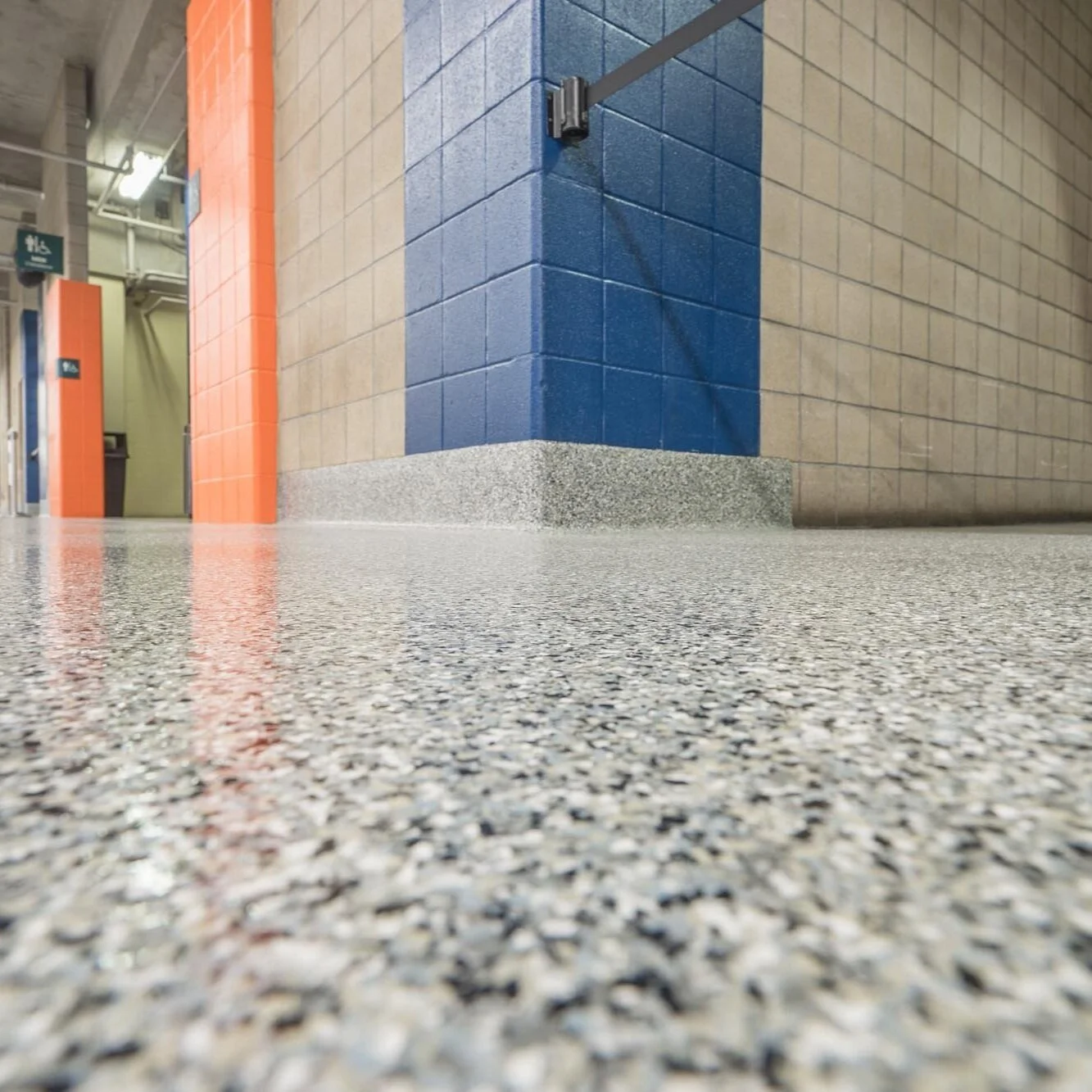 Low-angle view of polished speckled terrazzo floor and tiled walls in a public building with orange and blue accents.