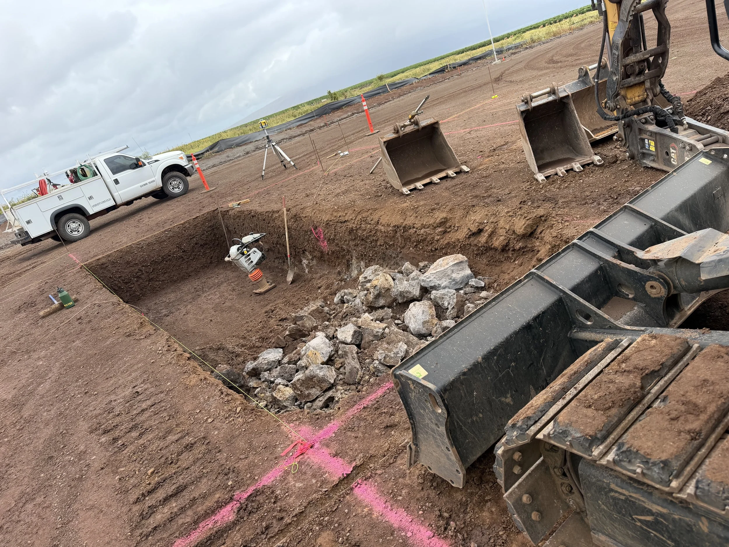 Construction site with excavation area, heavy machinery, and a pickup truck, under a cloudy sky.