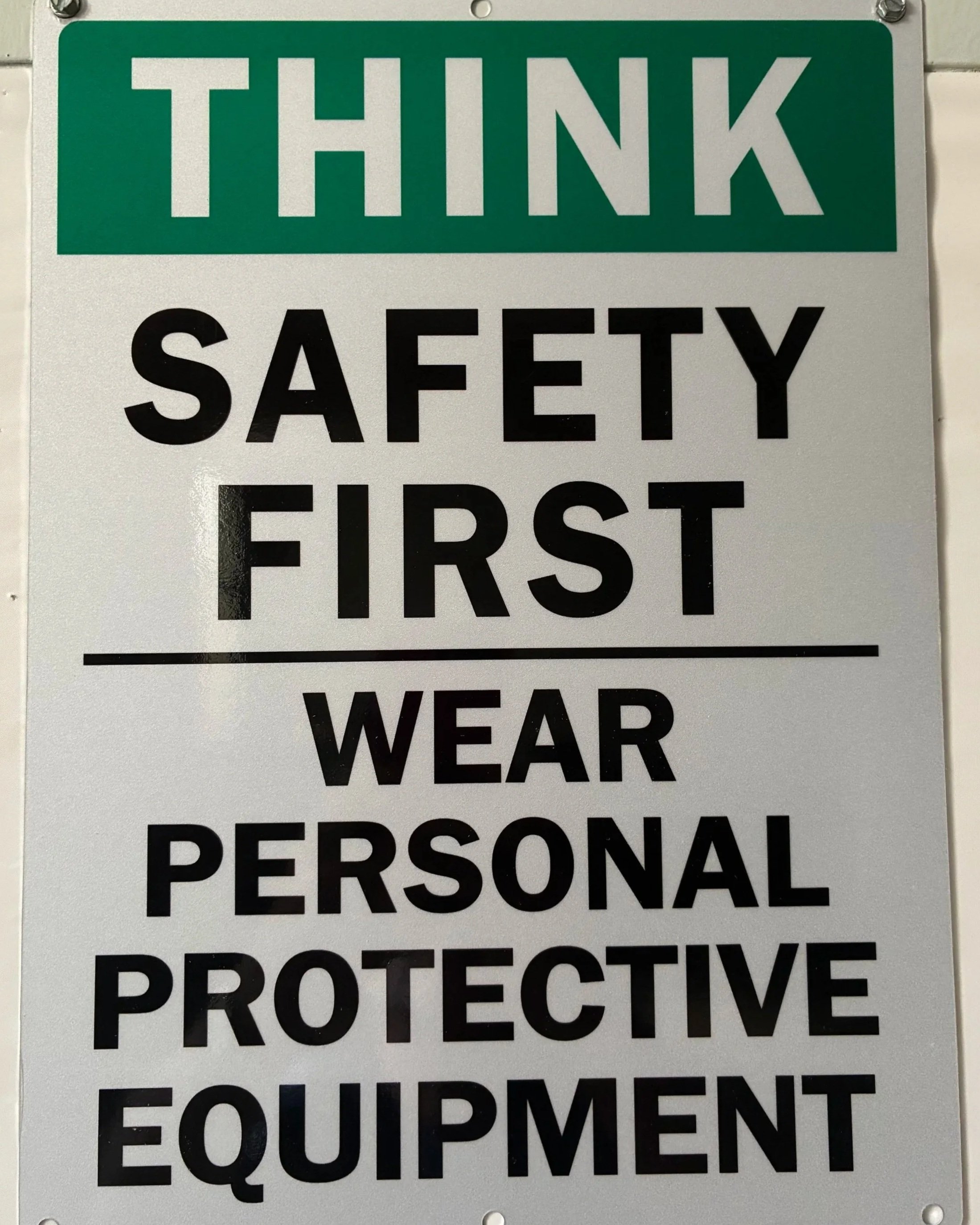 A safety sign with the word 'THINK' in large white letters on a green background at the top, and black text on a white background below that reads: 'SAFETY FIRST WEAR PROTECTIVE EQUIPMENT'.