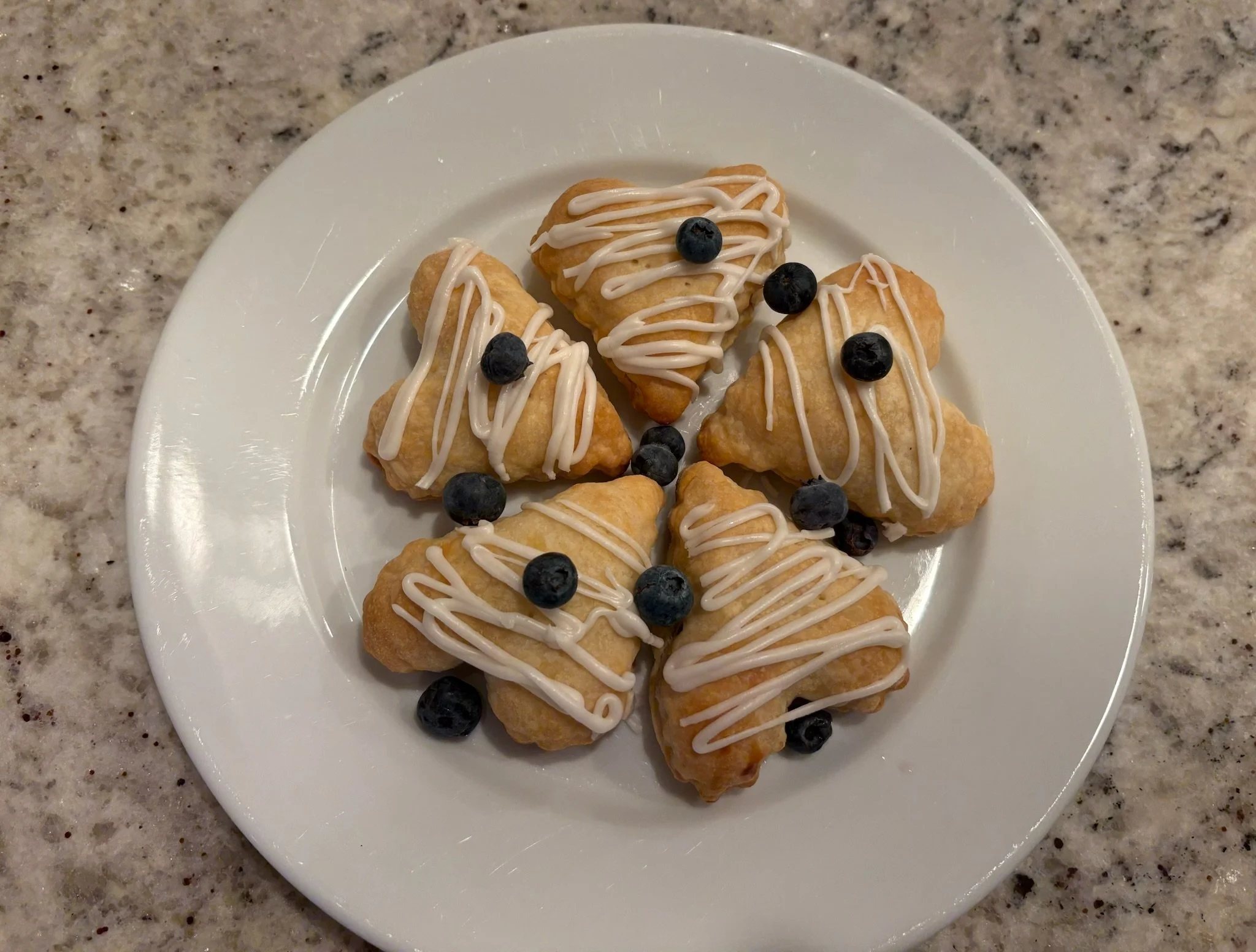 Plate with several small pastry bites drizzled with white icing and topped with blueberries.