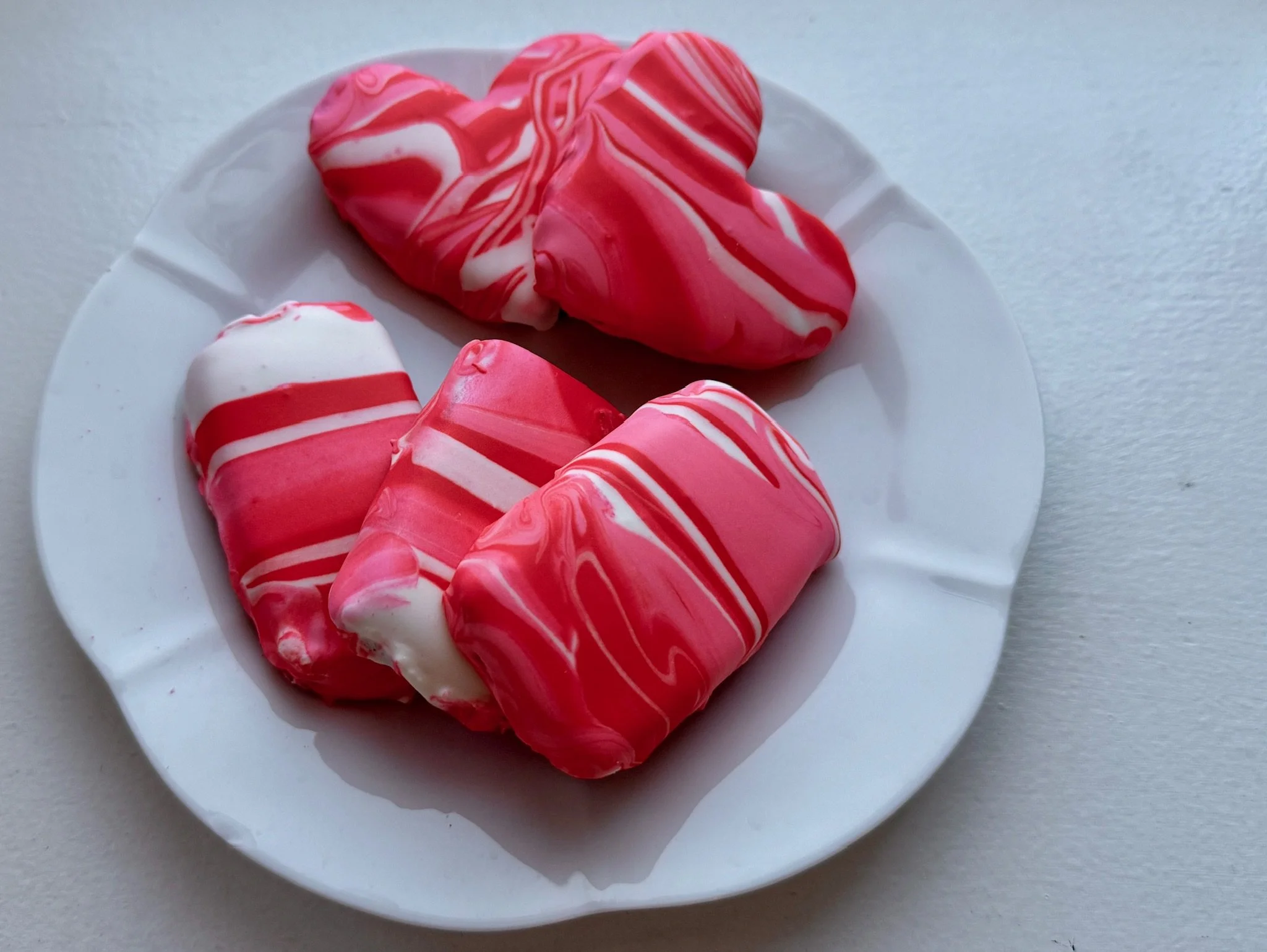 Several heart-shaped candies with red and white marbled swirl patterns on a white plate.