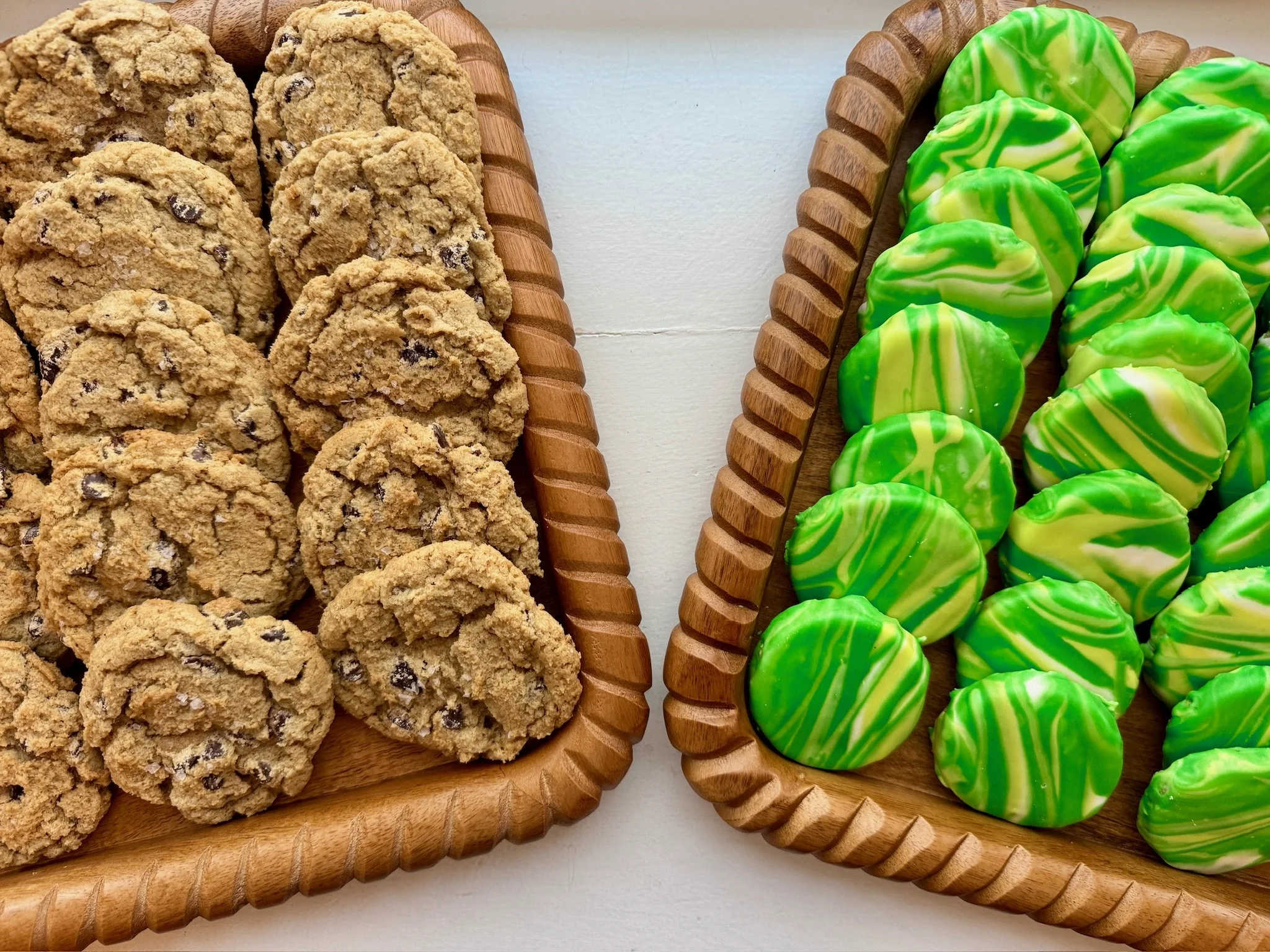 Two wooden trays filled with cookies on the left and green and yellow swirled candies on the right, placed on a white surface.