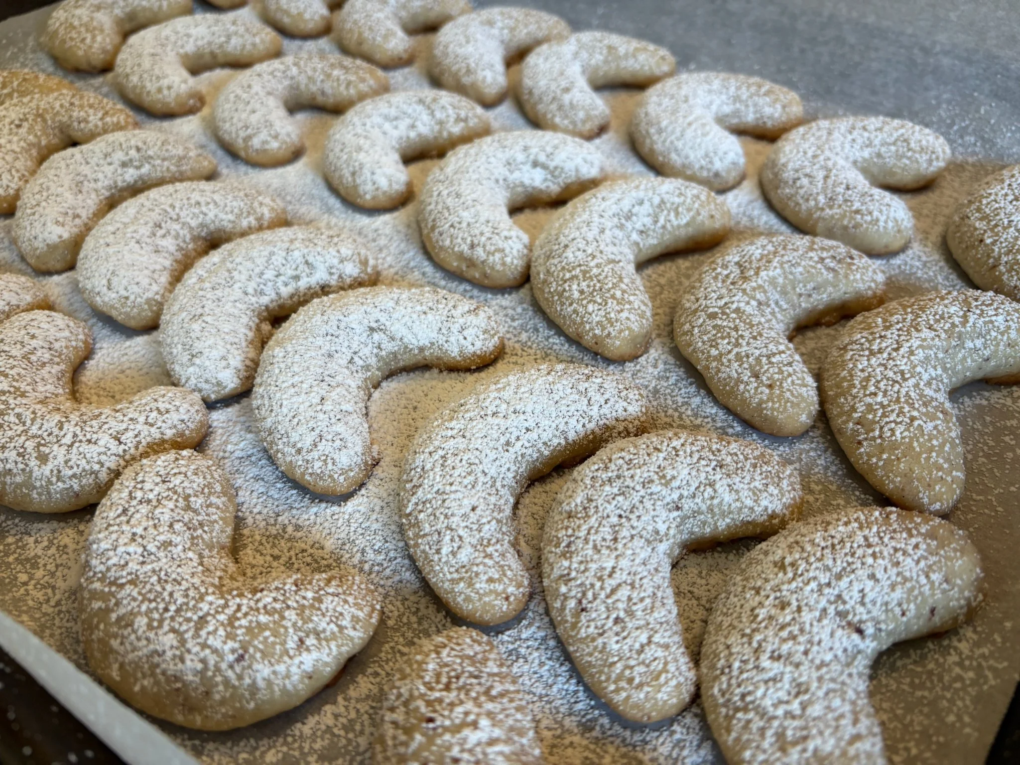 Unbaked crescent-shaped cookies dusted with powdered sugar on a baking sheet.