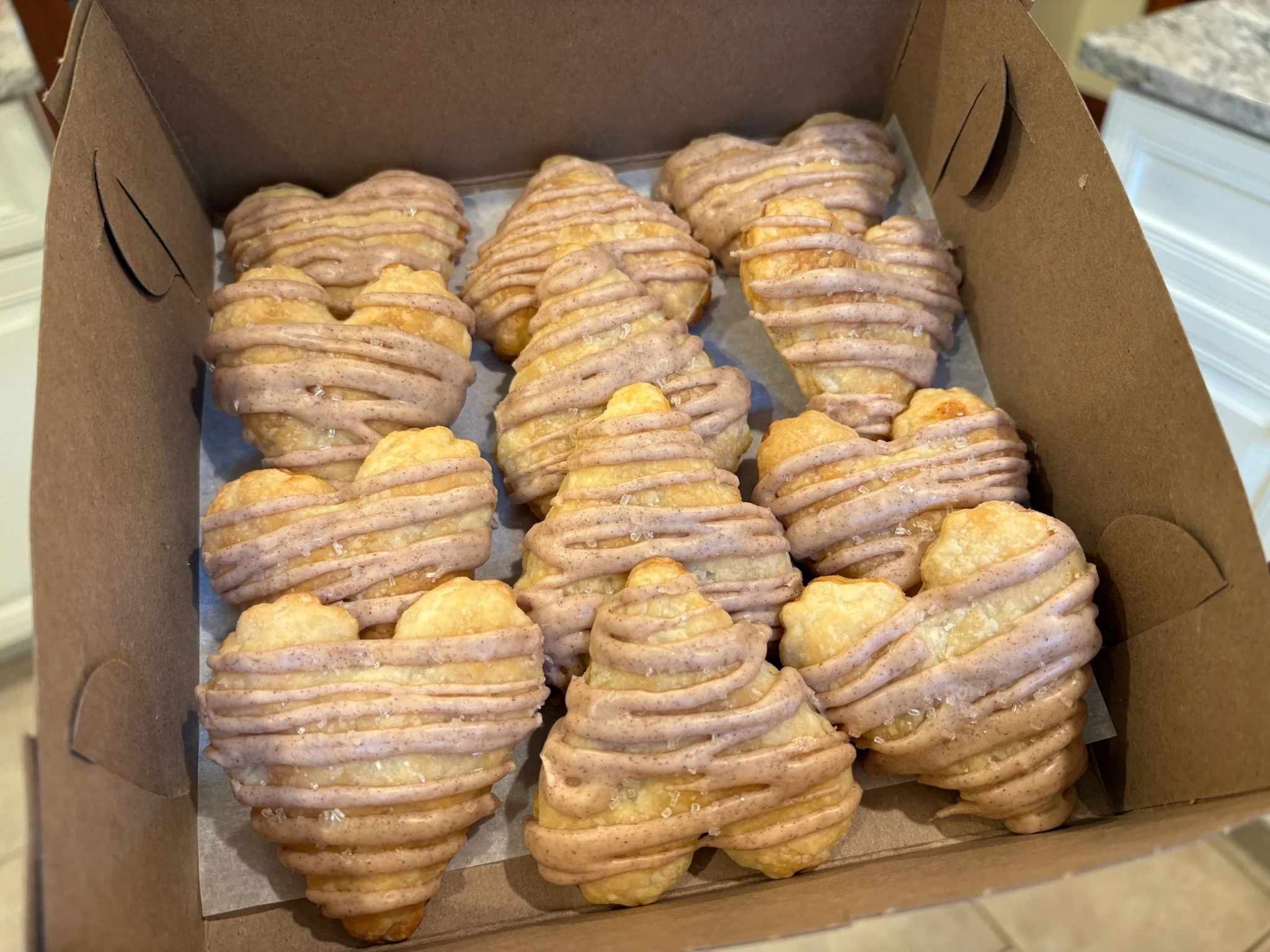 A cardboard box filled with assorted glazed donuts with drizzles of icing on top.