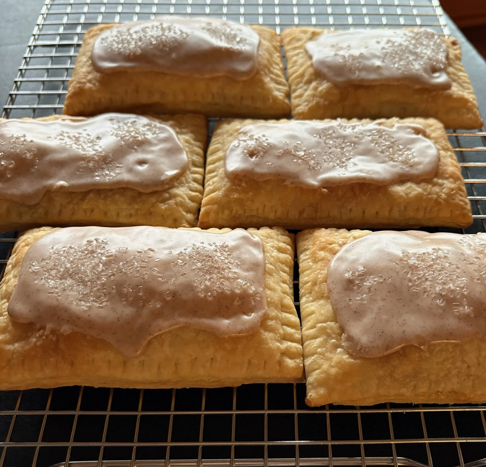 Four rectangular pastries with a golden-brown crust and white icing, sprinkled with shredded coconut, resting on a wire cooling rack.